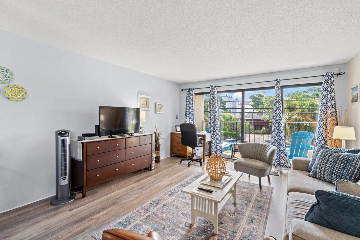 A bright, comfortable living room featuring a plush sofa, a coffee table, a streaming-capable TV as the entertainment focal point, and sliding glass doors that let in plenty of natural light. The overall atmosphere is cozy and homey, ideal for relaxing, watching TV, or gathering with friends and family.