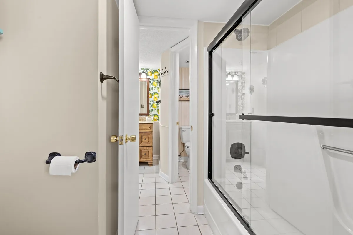 A modern bathroom with a glass shower enclosure, a stylish wooden vanity, and bright, leafy wallpaper that infuses the space with energy and freshness. The overall feel is clean, inviting, and functional.