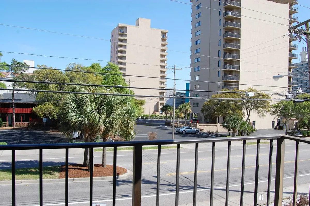 This image captures a lively street view lined with palm trees, framed by buildings that house local shops and restaurants. People are visible strolling along the sidewalks, adding a sense of activity and vibrancy to the neighborhood scene.