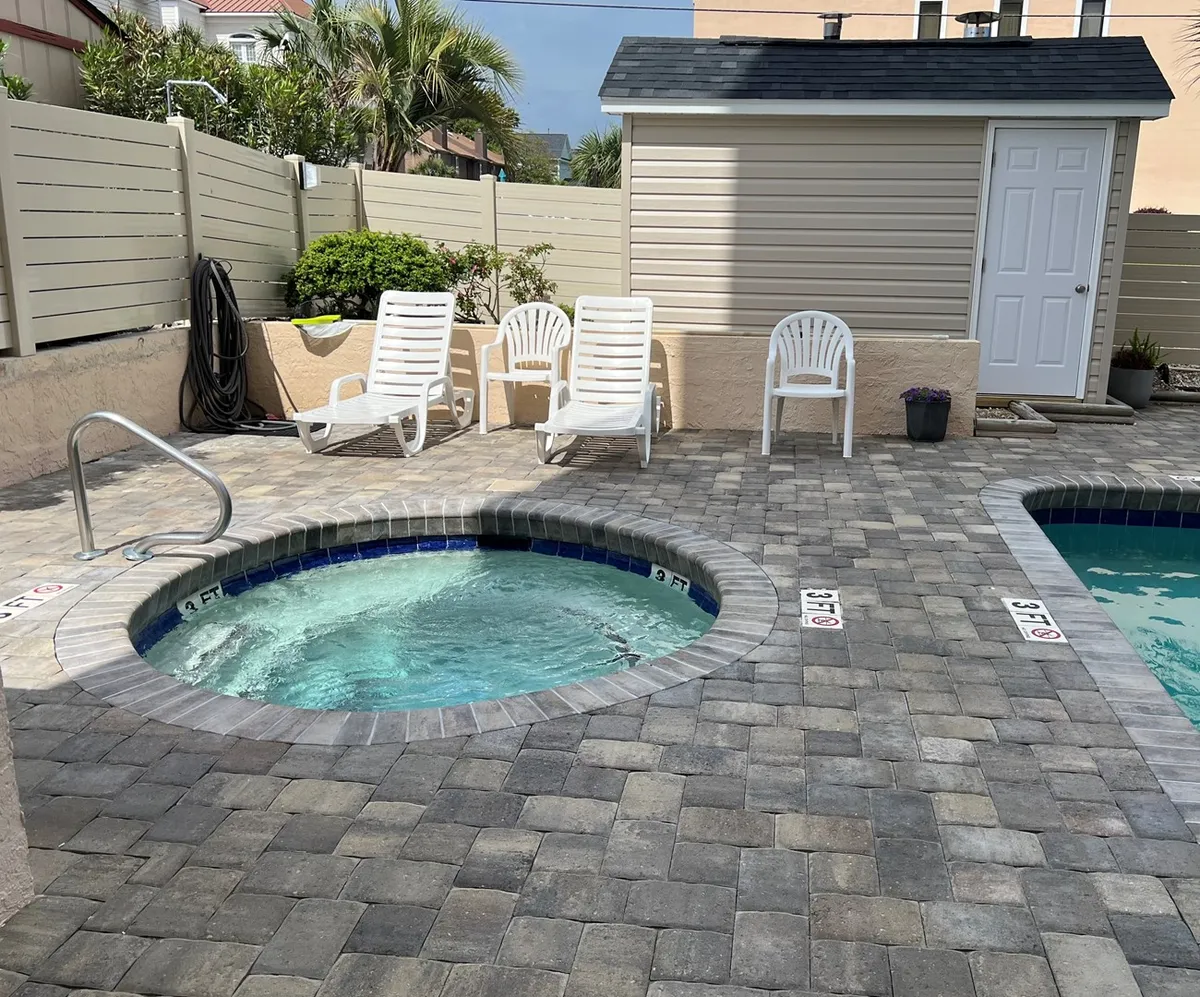 This exterior image showcases a vibrant patio area with a hot tub, lounge chairs, and a shed nearby. The sunlit space invites guests to unwind, socialize, or soak after a day of activities. The inviting atmosphere suggests family-friendly relaxation and communal fun, ideal for post-adventure downtime.