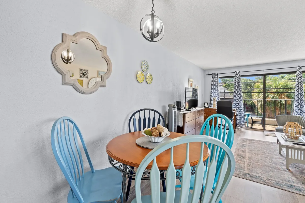 A cheery dining area with a wooden table, decorative mirror, TV in the background, and a potted plant for a touch of greenery. The tableau is set for shared meals, celebrations, or relaxed evenings at home, all within easy view of the main living space.