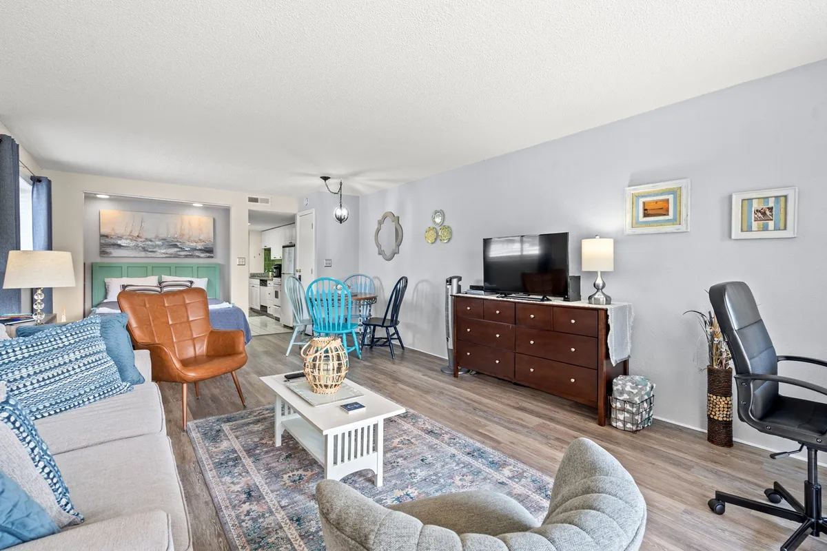 A spacious, open-plan lounge with a comfortable sofa, a coffee table, a large TV, decorative wall art, and dining chairs arranged nearby. The area is designed for both relaxation and entertaining, with a casual, lived-in feel that invites groups to gather for movies or games.