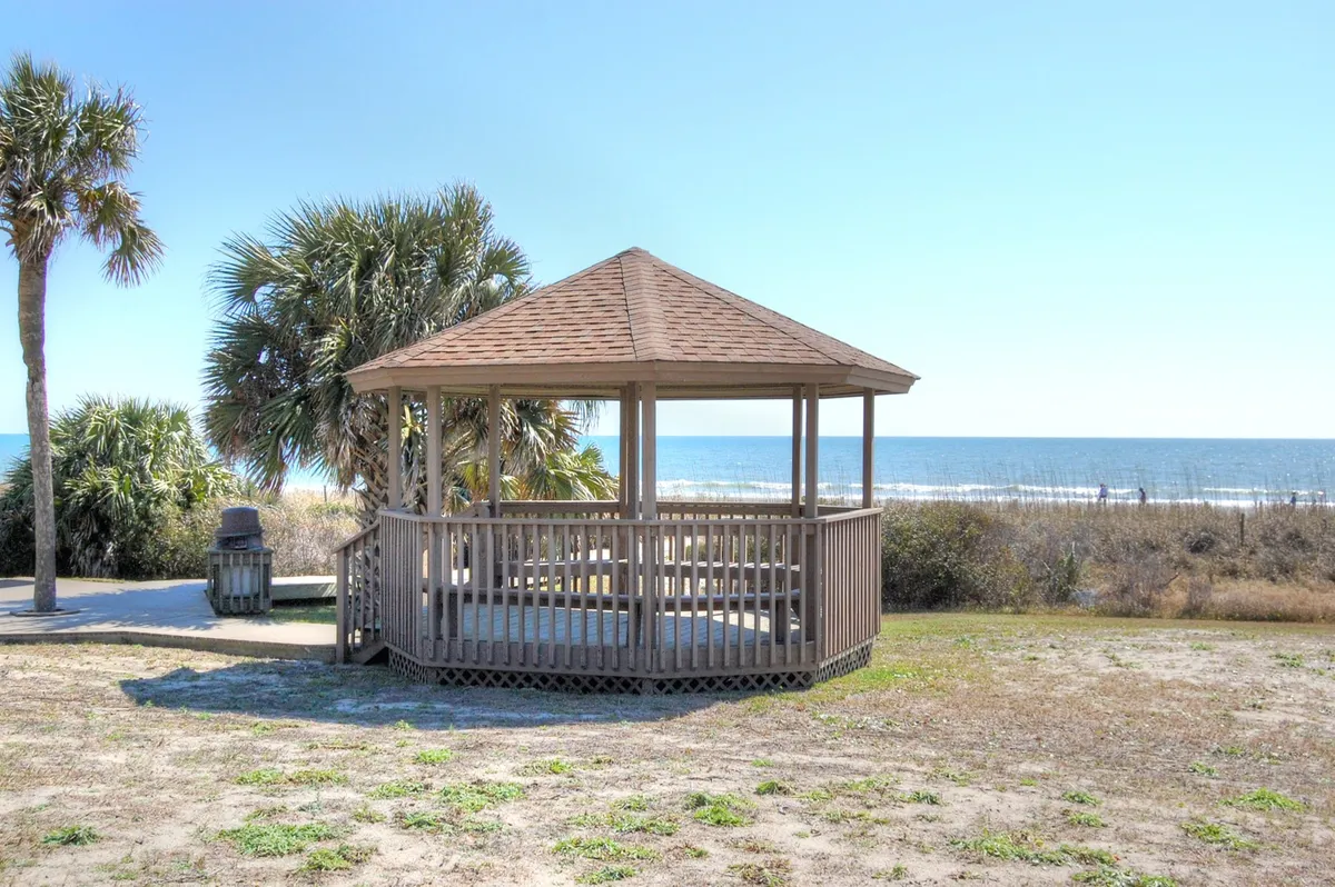 An inviting outdoor gazebo set against an ocean backdrop, surrounded by palm trees. The scene hints at opportunities for casual gatherings, sunset views, and peaceful moments before or after an evening out.
