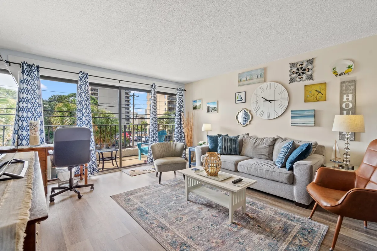 The image showcases a bright and inviting living area in the condo, featuring a comfortable sofa, stylish coffee table, tasteful wall art, and large windows that fill the space with warm natural light. The decor is modern yet cozy, creating a relaxing spot to unwind, socialize, or enjoy the view.