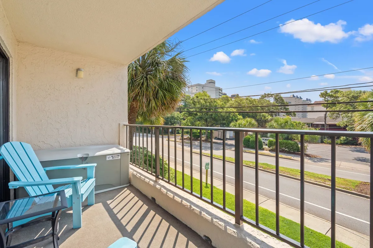 A tranquil exterior scene featuring balcony seating overlooking a palm-lined street. The view suggests a relaxing spot to enjoy coffee or an evening drink while soaking in the neighborhood’s ambiance and watching the sunset.